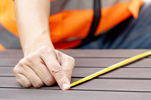 Ausschnitt einer Holzterrasse: Männerhände spannen ein Maßband zur Vermessung.
